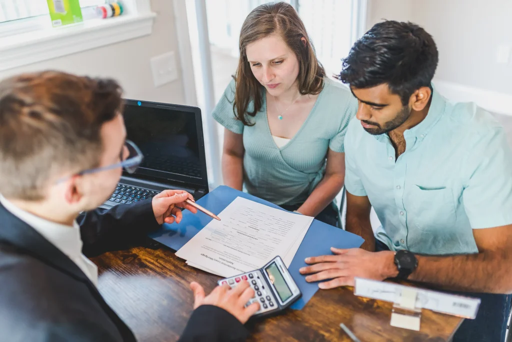 A couple speaking with an attorney looking at paperwork on the desk.
