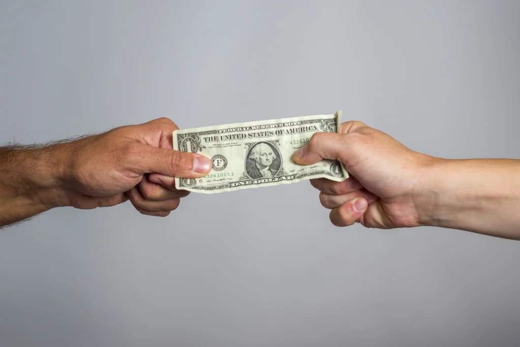 A dollar bill is help up by two people tensely holding each side of it.