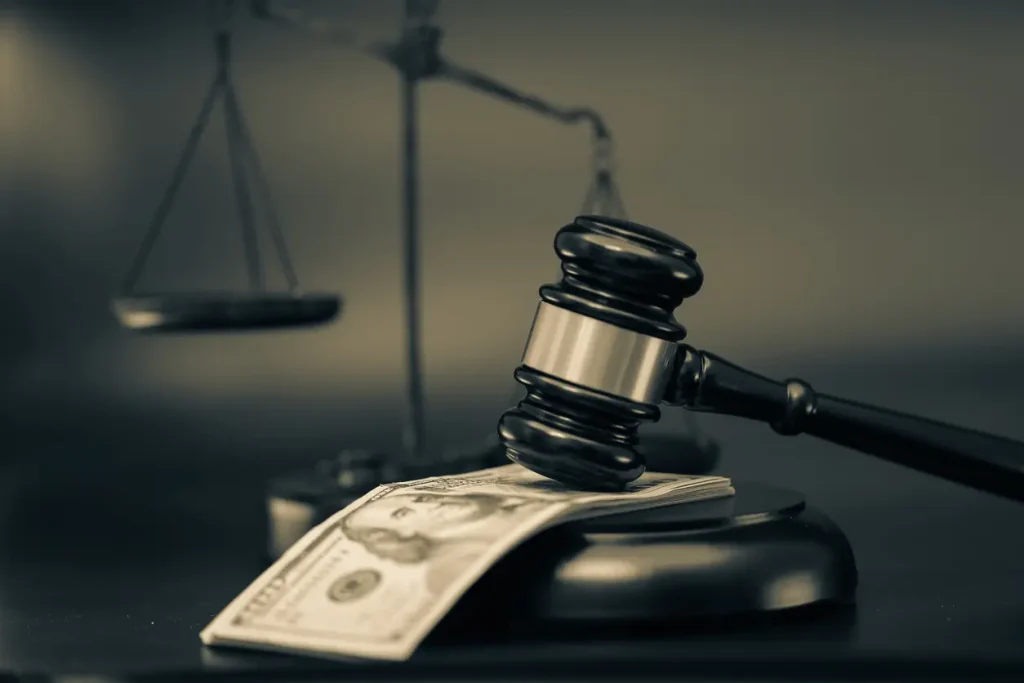 A pile of money sits under a gavel with a scale in the background.