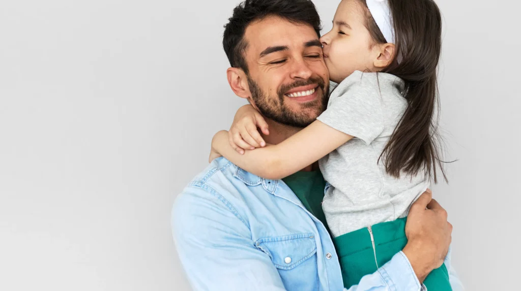 A dad hodling his daughter and smiling.
