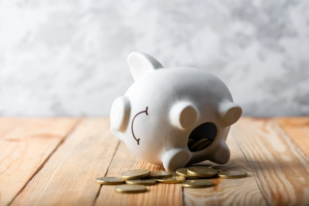 A tipped over piggy bank with coins spilling out.