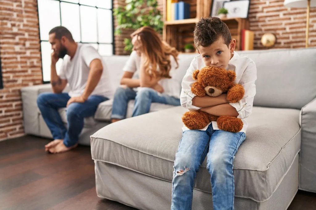Sad boy holding a teddy bear while parents argue.