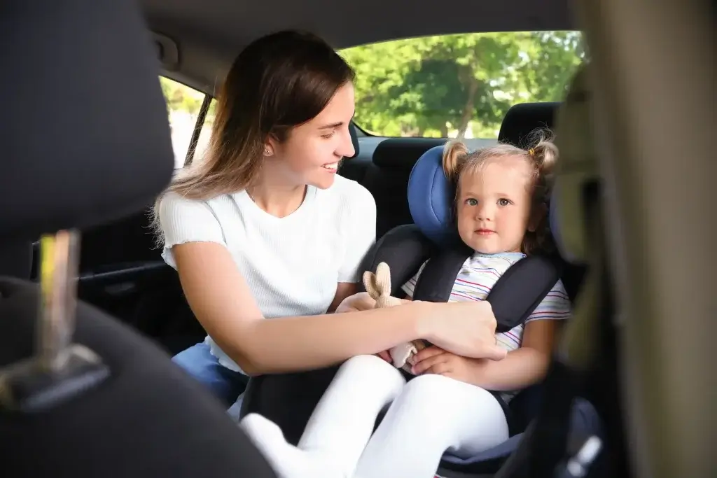 A mom buckling her daughter into her car seat.
