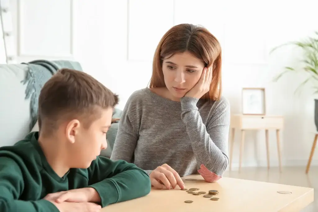 A concerned mother in Humble, Texas, counts coins on the kitchen counter while watching her son, highlighting the financial strain families face when child support enforcement is delayed or ignored.