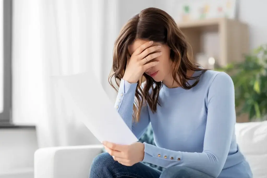A distressed woman sits on a couch in Texas, covering her eyes while reading a legal document—capturing the frustration and emotional strain of dealing with an ex who fails to follow a finalized divorce agreement.