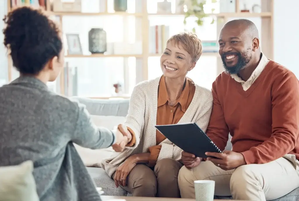 Smiling couple holding paperwork and shaking hands, showing how Farias Law Firm supports estate planning after inheriting property in Texas.